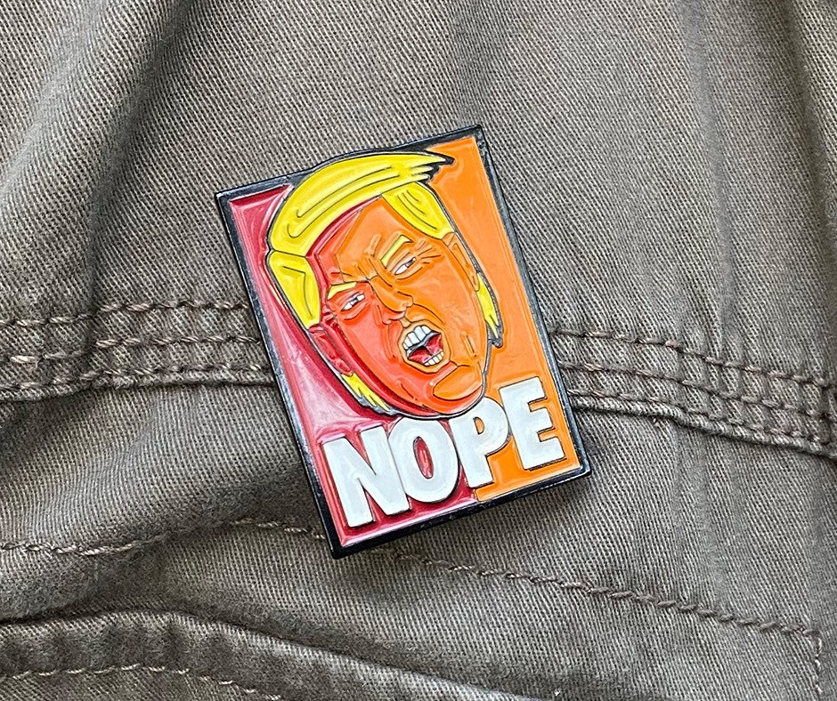 NOPE enamel pin worn on an olive green army jacket